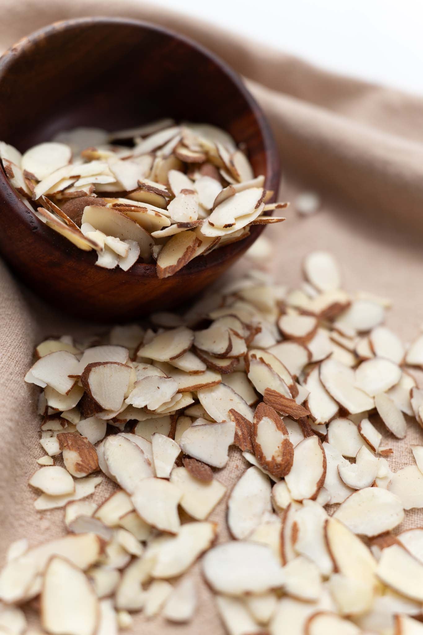 Wooden bowl half filled with raw sliced almonds spilling out