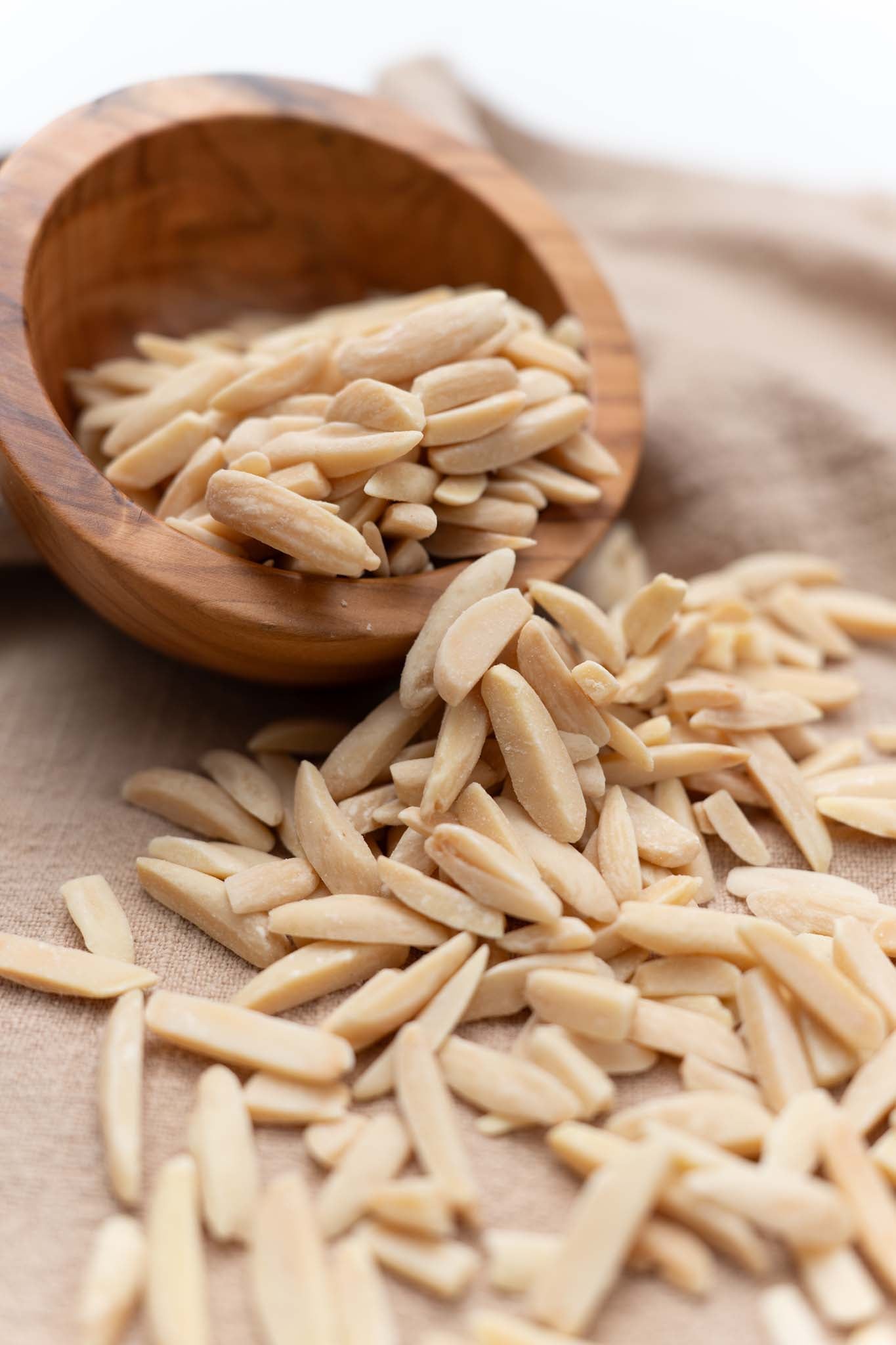 Wooden bowl half filled with roasted slivered almonds spilling out